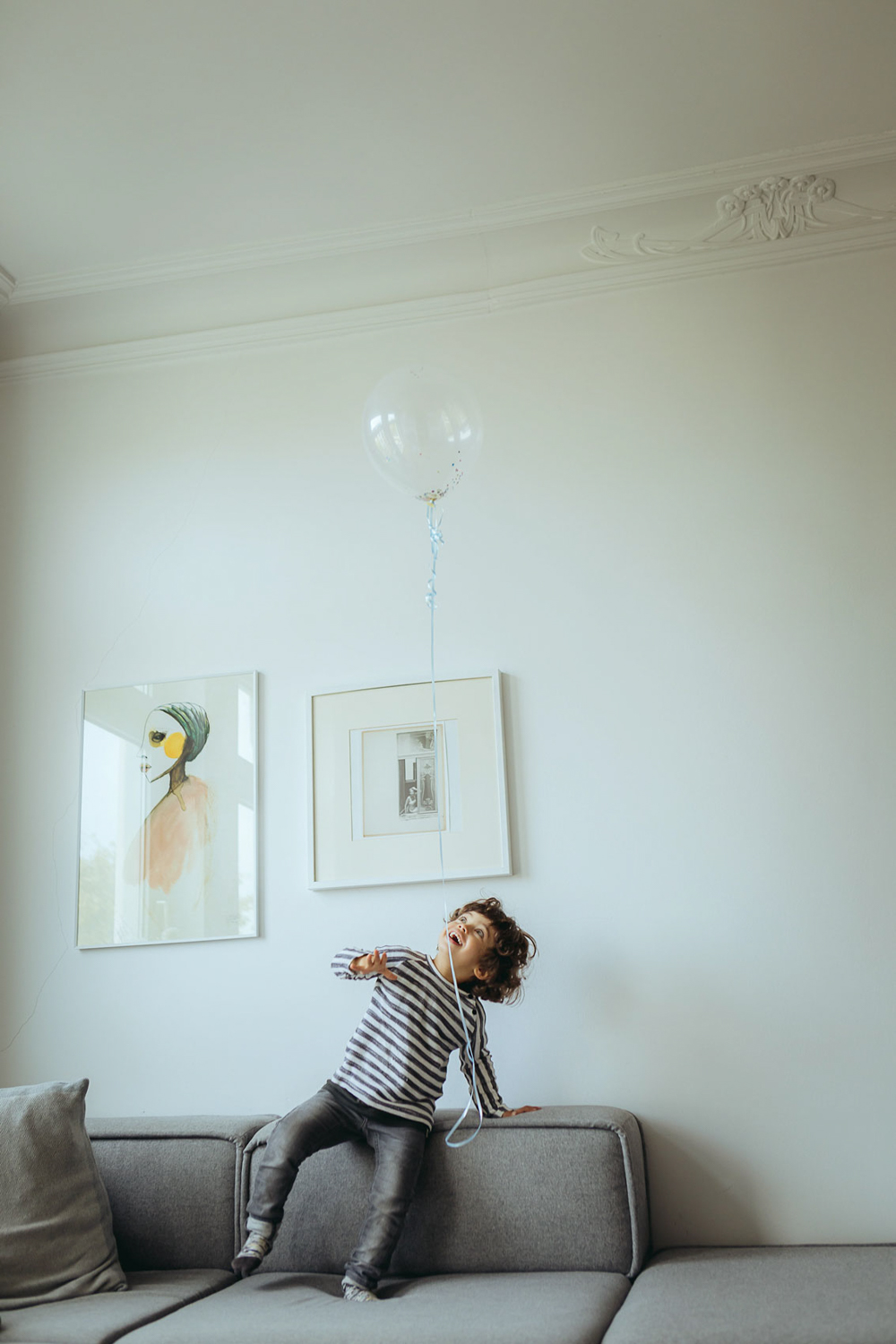 Kind spielt mit Luftballon im Wohnzimmer auf Couch