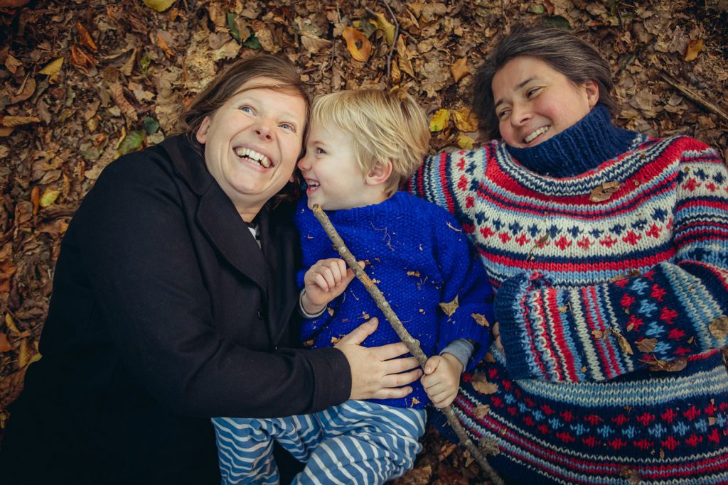 Zwei Frauen liegen ausgelassen mit ihrem Sohn auf dem Waldboden im Laub