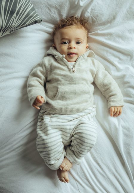 Baby in heller Kleidung auf Familienbett